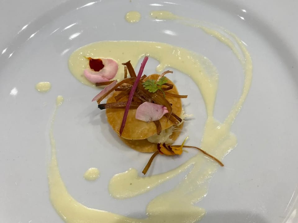 Entrada: emulsión de coliflor con pétalos comestibles sobre plato blanco.
