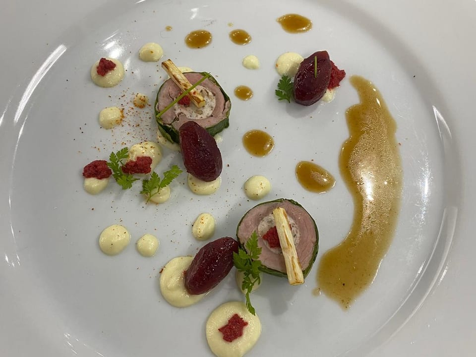 Plato principal: roulade de carne con puré de remolacha y guarniciones de hierba.